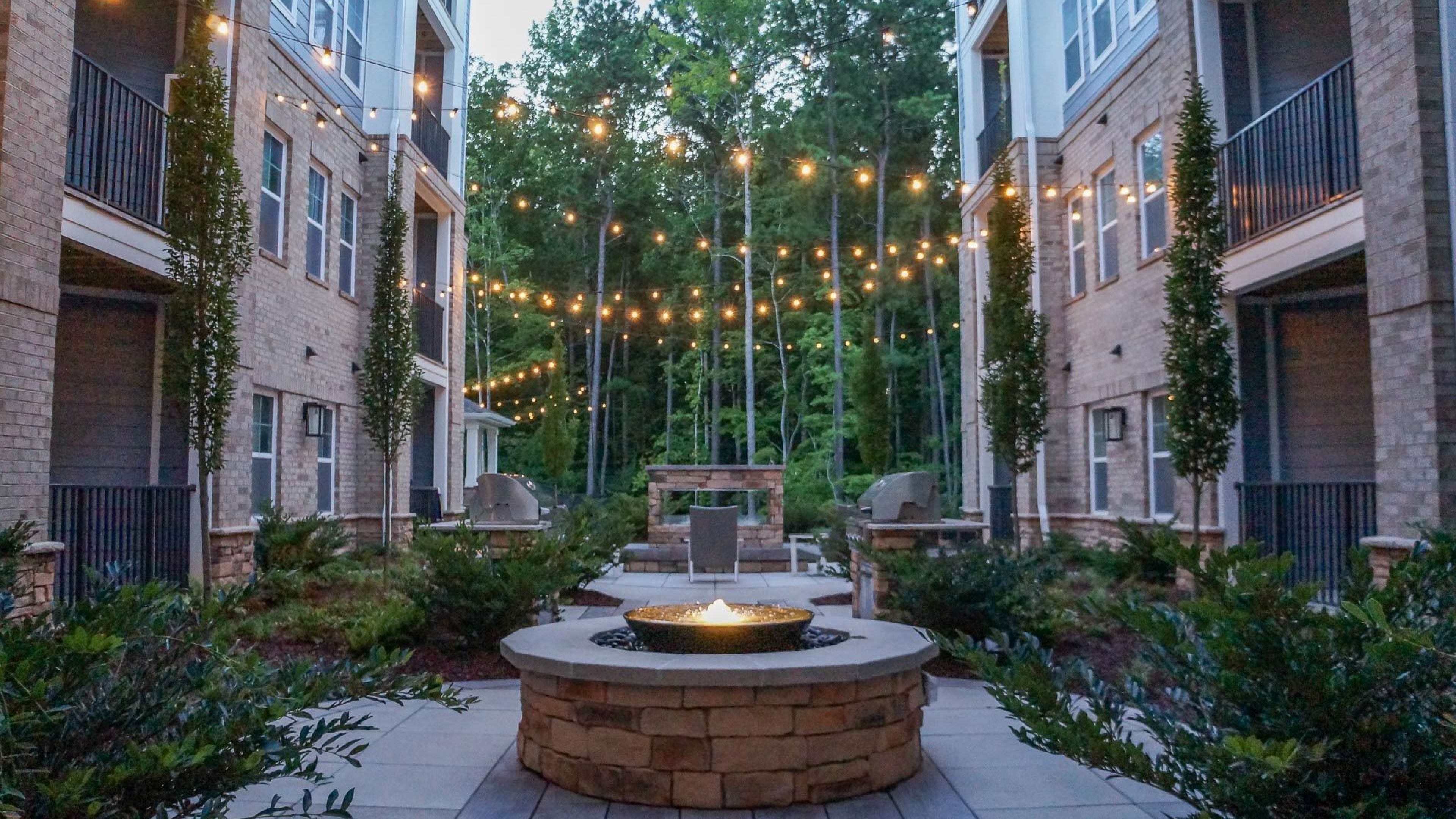 Hawthorne at Parkside beautiful outdoor courtyard amenity with a grill area and firepit, overhanging lights drape across the courtyard
